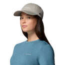 A person wearing a light gray Columbia Provisions Ball Cap with an adjustable back closure and a blue Columbia T-shirt looks at the camera against a plain white background.