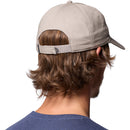 A person with wavy brown hair is seen from behind, wearing a beige Columbia Provisions Ball Cap and a blue shirt. The adjustable back closure of the cotton cap is visible.