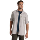 Man wearing a light gray short-sleeve shirt over a dark blue t-shirt on a beige background