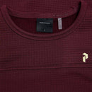 Close-up of the Peak Performance Womens Trail Polartec Power Grid Crew Fleece in maroon, made from textured Polartec Power Grid fabric, showcasing a visible Peak Performance label inside the collar and a small gold geometric logo on the chest—an ideal pullover for your next outdoor adventure.