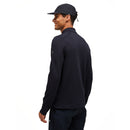 A man wears the Peak Performance Mens Trail Polartec Power Grid Half Zip Fleece in black, paired with a black cap, as he stands against a plain white background, facing slightly away and smiling.