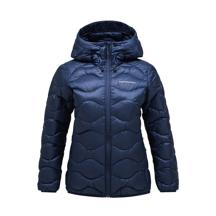 The Womens Helium Down Hood Jacket by Peak Performance is a navy blue puffer with a hood, front zipper, and subtle wavy stitching. It features a windproof, water-repellent shell and is displayed against a plain white background.