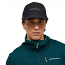 A person wearing a black Peak Performance cap and the Men’s Trail Polartec Power Grid Zip Hooded Fleece by Peak Performance in teal, styled as a technical midlayer, looks directly at the camera against a plain white background.