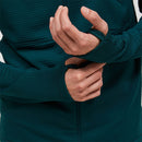 A person wearing the Peak Performance Mens Trail Polartec Power Grid Zip Hooded Fleece in dark green, featuring a textured fabric and thumb holes, adjusts the sleeve of their other arm.