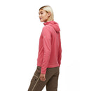 A person with short blond hair wears the Peak Performance Womens Trail Polartec Power Grid Zip Hooded Fleece in pink and brown pants, standing turned slightly to the side against a plain white background.