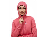 A woman wears the Peak Performance Womens Trail Polartec Power Grid Zip Hooded Fleece in pink, holding the partially zipped neckline near her chin and gazing to the side against a plain white background. This technical midlayer features innovative Polartec Power Grid construction, making it ideal for active adventures on the trail.
