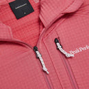 Close-up of the Peak Performance Womens Trail Polartec Power Grid Zip Hooded Fleece in pink, showcasing the brand logo, zipper pulls with white cords, a textured Polartec Power Grid fleece interior, and a black size S tag.