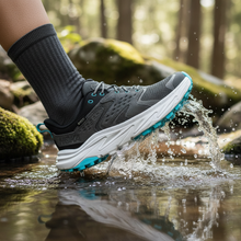 Person wearing a gray and blue HOKA waterproof shoe stepping into water in a forest setting