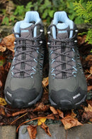 A pair of Meindl Womens Journey Mid GTX Walking Boots in gray and blue are placed side by side on the ground amid brown leaves and greenery, highlighting their waterproof design perfect for any outdoor adventure.