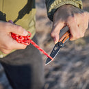 A person in an olive green jacket uses the Leatherman Skeletool® KB Knife with a 420HC stainless steel blade to cut a red rope outdoors.