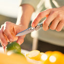 Someone slices a green lime on a white surface using the Leatherman Skeletool® KB Knife, with yellow citrus fruits in the foreground.
