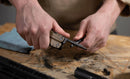 At a workbench scattered with tools, metal shavings, and a blue cloth, someone uses the Leatherman Super Tool® 300M - Molle Black for firearm maintenance on a small metal part.