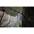 A gloved hand uses a Leatherman Surge Multitool with pliers to grip barbed wire attached to a wooden post outdoors.