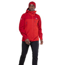 A man in a red Mountain Equipment Mens Lhotse GTX Pro Jacket, red beanie, and black pants stands against a white background, looking to the side with one arm slightly bent.