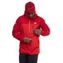 A man in a red Mountain Equipment Mens Lhotse GTX Pro Jacket and matching beanie looks down while unzipping a chest pocket, standing against a white background.
