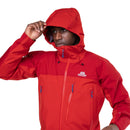 A person wearing a Mountain Equipment Mens Lhotse GTX Pro Jacket in bright red, adjusting the hood with zippered pockets visible, stands against a white background.