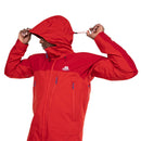 A person adjusts the hood of a Mens Lhotse GTX Pro Jacket by Mountain Equipment, a bright red GORE-TEX Pro jacket with blue zipper accents and the Mountain Equipment logo on the chest, while facing sideways.