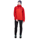 A woman modeling a red and orange two-tone outdoor jacket, paired with black pants and a dark beanie, against a plain white background.