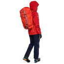 A person wearing a red hooded jacket, navy pants, and hiking boots, shown from the back while wearing a bright orange hiking backpack against a white background.