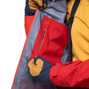 Close-up of a person wearing a colorblock winter jacket with red, navy, and yellow sections, showing a zippered pocket and gloved hands.
