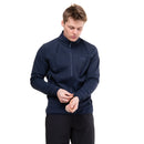 A man wearing the Mountain Equipment Men’s Jorasses Lite Fleece Jacket in navy blue and black pants stands against a white background, adjusting the sleeve of his lightweight mid-layer while looking down.