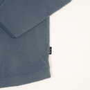 Close-up of a textured fleece garment in a muted slate blue color, showing the soft sherpa fabric and a small black brand tag on a plain white background.