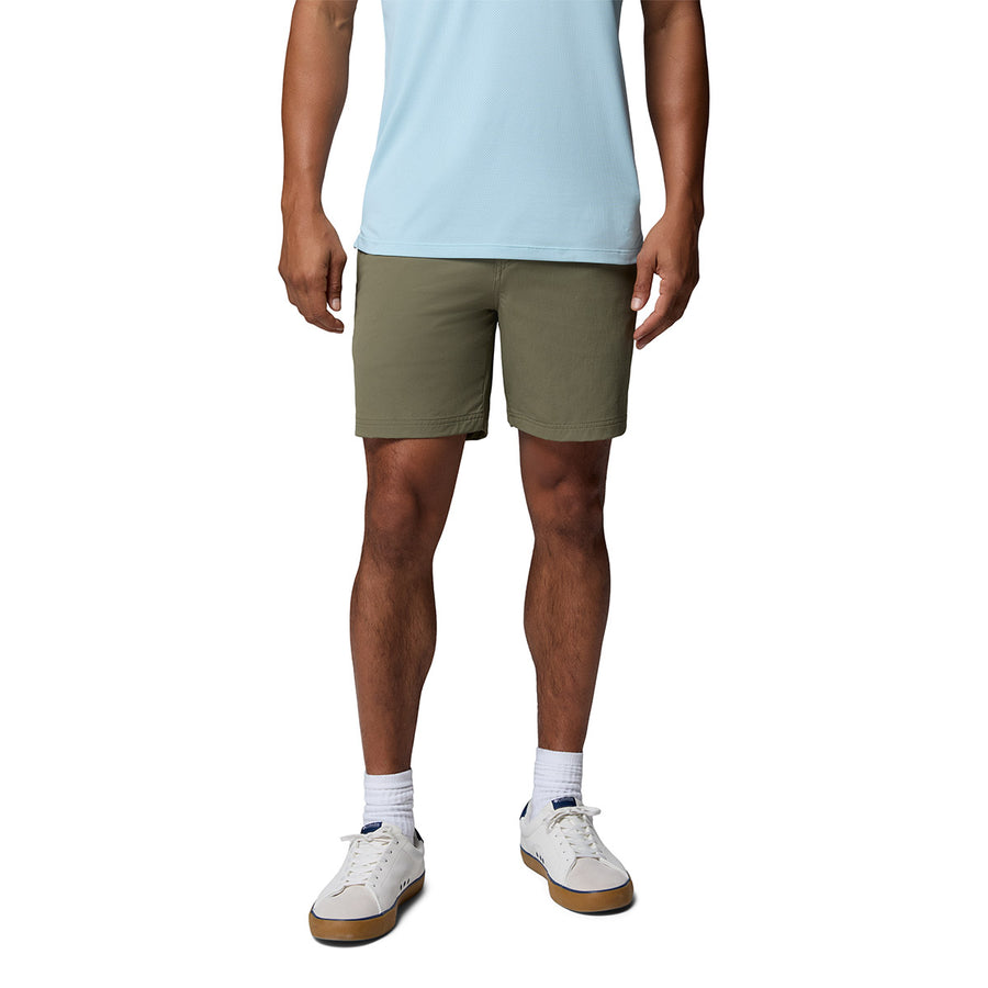 A person wears a light blue shirt, Columbia Mens ROC Tech Shorts in olive green, white crew socks, and white sneakers with gray accents, standing against a plain white background. The photo captures them from shoulders to feet.