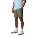 A person in a light blue shirt, Columbia Mens ROC Tech Shorts in olive green, white socks, and white sneakers stands with hands in pockets against a plain background.
