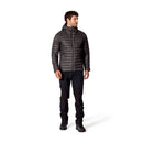 A man wearing a black Rab Men’s Microlight Alpine Hoody, black pants, and black boots stands facing slightly left against a white background. This jacket features recycled down insulation for both warmth and sustainability.