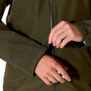A person adjusts the Velcro strap on the cuff of a green Rab Mens Namche GTX Waterproof Jacket sleeve, with both hands visible and part of a zipper in the center of the jacket.
