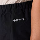 Close-up of a person wearing black Rab Mens Namche Hike GORE-TEX Pants, featuring the white GORE-TEX logo printed on the side near their arm. These mens waterproof pants by Rab are designed to provide reliable protection and performance in any weather.