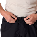 A person wearing a white shirt adjusts the drawstring at the waist of Rab Mens Namche Hike GORE-TEX Pants in black, with the focus on their hands and waist.