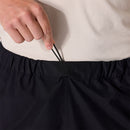 A person adjusts the drawstring on the waistband of Rab Mens Namche Hike GORE-TEX Pants in black while wearing a light-colored, textured shirt.
