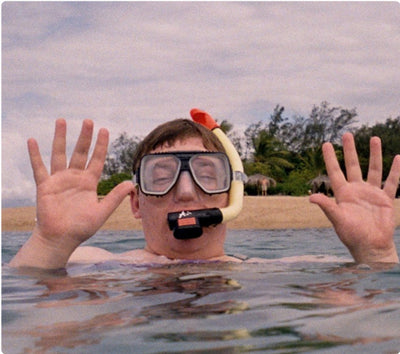 man swimming at the beach wearing snorkel and goggles with his hands up