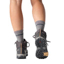A person walking, shown from behind, wearing gray Salomon socks and dark gray Womens X-Ultra 5 Mid GORE-TEX Hiking Boots with rugged soles and a durable Matryx upper on a white background.