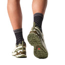 A close-up rear view of a person walking in black patterned socks and green Salomon Mens XA Pro 3D V9 GORE-TEX Trail Shoes, ideal for technical terrain, isolated on a white background.