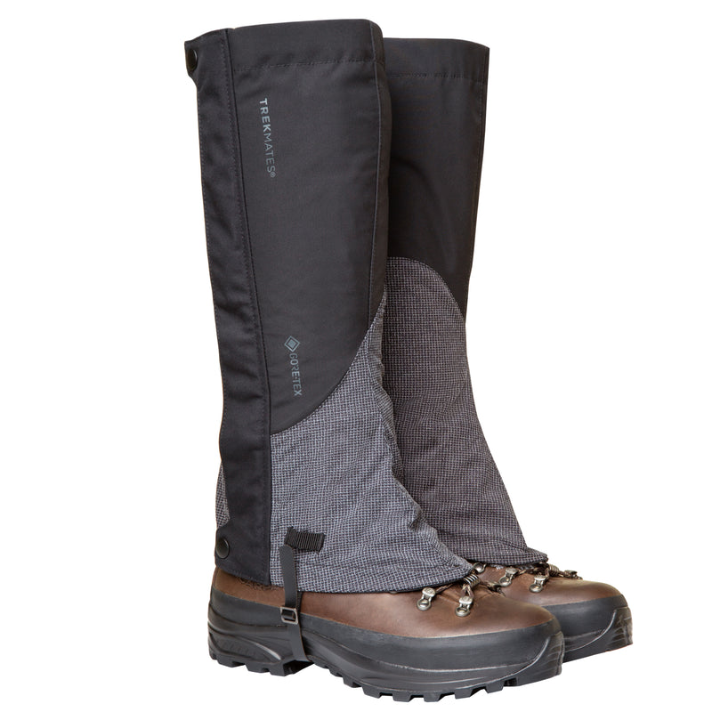 A pair of brown hiking boots fitted with Trekmates Cuillin GORE-TEX Gaiters in black and gray, designed to protect against water, dirt, and debris during mountain walks. These gaiters feature the Trekmates logo and provide coverage for the lower leg and upper boot area.