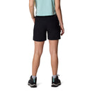 A person is standing facing away, wearing a light turquoise shirt, Columbia Womens Cedar Crest Hiking Shorts, gray socks, and black athletic shoes against a white background.