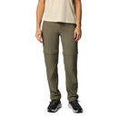 A person wearing Columbia Womens Leslie Falls Hiking Convertible Trousers in olive green with Omni-Shield technology, a beige short-sleeve shirt, and black sneakers stands against a white background. The trousers zip off at the knees to convert into shorts.