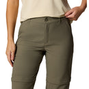 A person wears Columbia Womens Leslie Falls Hiking Convertible Trousers and a light beige t-shirt, standing with one hand in their pocket and the other on the waistband. The photo is cropped at the chest and upper thighs.
