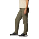 A person wearing Columbia Womens Leslie Falls Hiking Convertible Trousers stands sideways against a white background, paired with a beige shirt and black athletic shoes. Only the lower half of the body is visible.