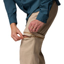 A person in a teal long-sleeve shirt and Columbia Womens Leslie Falls Hiking Convertible Trousers is unzipping the pants at the knee to convert them into shorts.