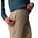 A person in Columbia Womens Leslie Falls Hiking Convertible Trousers is unzipping the front pocket. Only the torso and upper legs are visible, highlighting these teal and beige pants versatility and Omni-Shield technology.