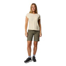 A woman stands facing forward, smiling, in a light beige t-shirt and Columbia Womens Leslie Falls Hiking Convertible Trousers, gray socks, and black sneakers against a plain white background.