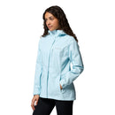 A woman wears a light blue Columbia Womens Pouring Adventure III Waterproof Hiking Jacket, hands in pockets, standing against a plain white background.