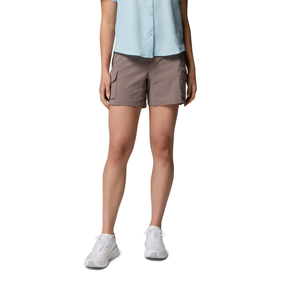 Wearing a light blue short-sleeve shirt, Columbia Womens Silver Ridge Elite Hiking Shorts in taupe, and white sneakers, a person stands against a white background. Their face is not visible.