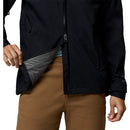 A person, visible from the waist down, unzips a Columbia Womens Trailborne 2.5L Waterproof Shell Jacket to reveal its patterned lining while wearing brown pants. Only their lower body and one hand are shown.
