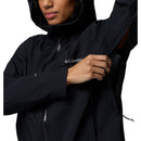 A woman in a black Columbia Womens Trailborne 2.5L Waterproof Shell Jacket with a hood unzips the underarm vent; only her lower face and upper body are visible.