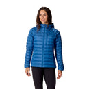 A woman wearing the Rab Womens Microlight Alpine Hoody in blue with the hood up and black pants, standing and smiling against a white background.
