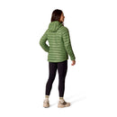 A woman stands with her back to the camera, wearing the Rab Womens Microlight Alpine Hoody in green, paired with black leggings and beige hiking boots, against a white background.